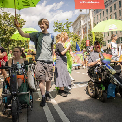 Verschiedene Menschen mit grünen Schirmen auf der Regenbogenparade