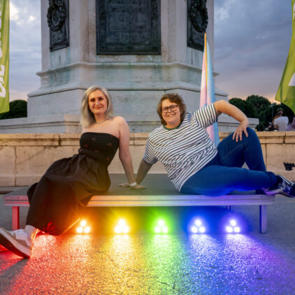 Zwei Personen (Grüne Andersrum Wien Sprecher:innen Katharina Schöll-Laussermayer und Nikki Ullrich) vor Regenbogen-Lichtinstallation.