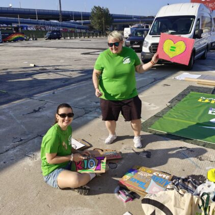 Zwei Personen bemalen Schilder auf dem Boden, eine hält ein Herz-Plakat.