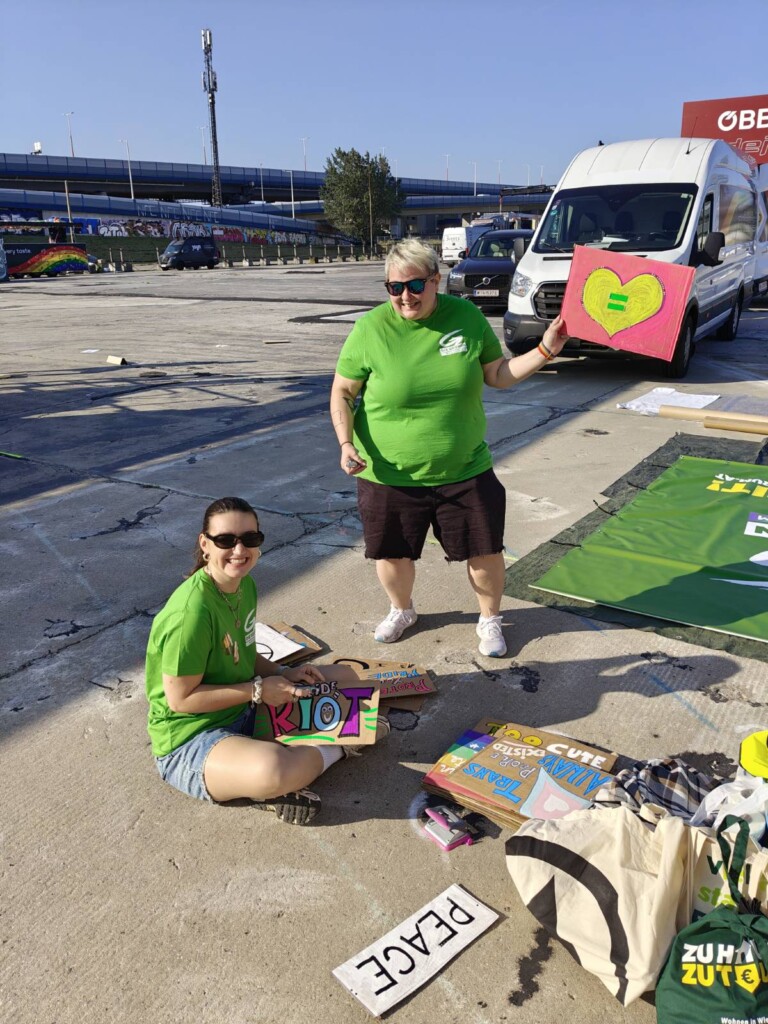 Zwei Personen bemalen Schilder auf dem Boden, eine hält ein Herz-Plakat.